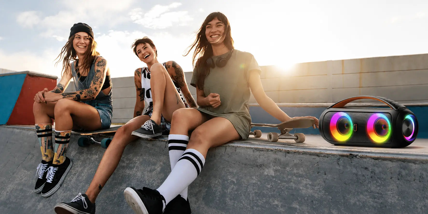 black jyx d16t portable speaker with multicolor light rings and a carry handle beside friends and skateboards at a skatepark.